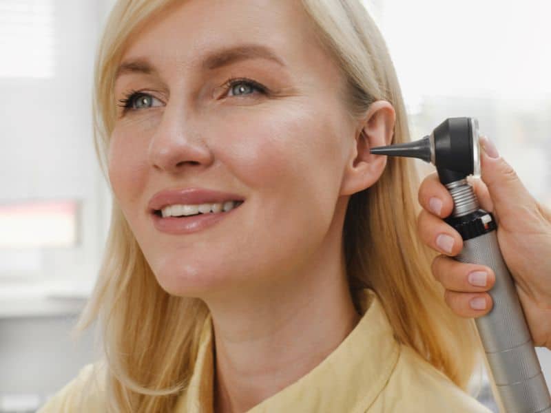 woman smiling while otoscope looks in ear